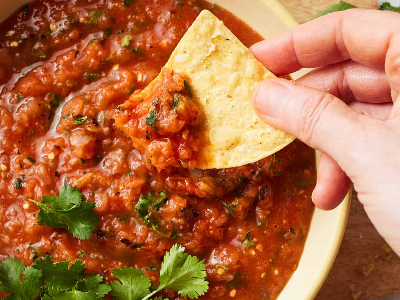 A close up shot of red salsa with a hand dipping a tortilla chip in it