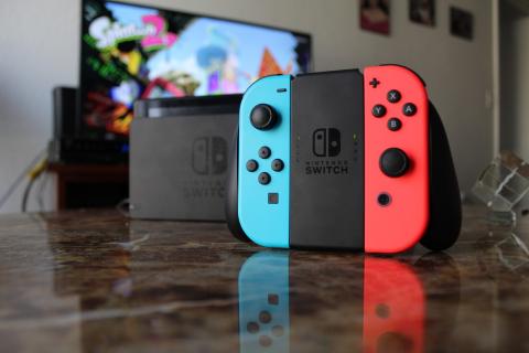 a blue and red Nintendo switch controller is in the foreground, with a tv showing a video game image in the background
