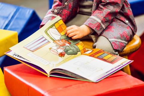 Close up of an open picture book with a toddler's hands resting on the pages, holding it open.