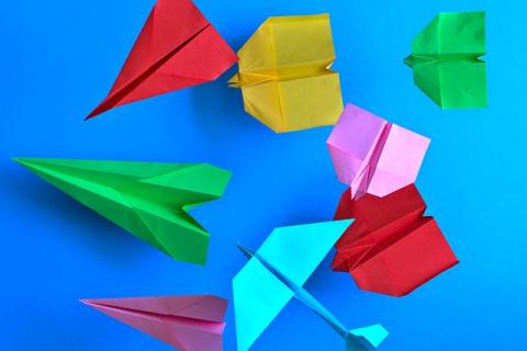 Paper airplanes in the colors green, light blue, pink, red, and yellow on a bright blue background..