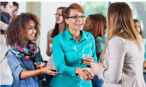 A diverse trio of adults are smiling as they greet and mingle with each other.