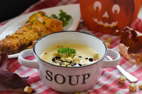 a cup that says SOUP on the side full of white potato soup on a red checked tablecloth