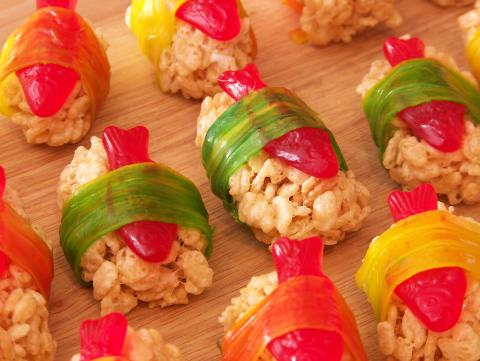 rows of sushi made out of rice krispie treats with swedish fish, wrapped in fruit candy