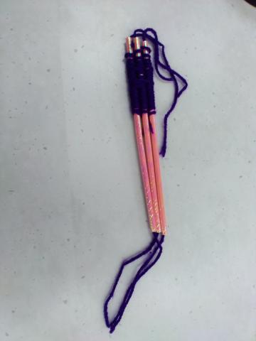 Three shiny pink paper straws with purple yarn woven onto them.