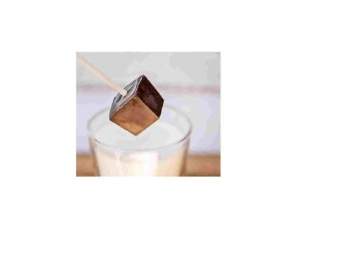 A wooden stick inside a dark chocolate cube hovering above a glass filled with milk.