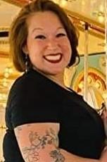 Photo of author Maria Des Jarlait, a woman with medium-length brown hair, and tattoo on her right arm