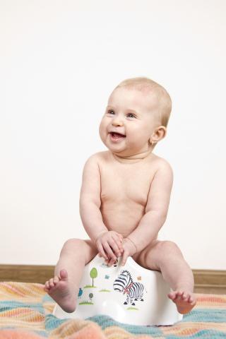 A photo of a laughing baby sitting on a potty chair that is decorated with whimsical animals.