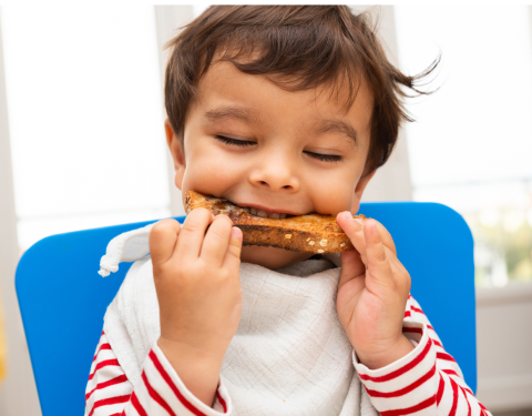 A young boy with slightly mussed dark hair bites into a piece of toast