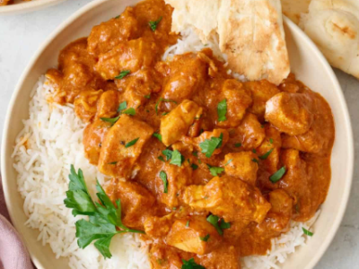 close up on a bowl of white rice with orange colored chicken and sauce on top