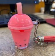 a cute pink miniature bubble tea attached with a keychain to a pink stylus on a granite colored surface