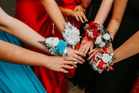 many hands from different teens in formal dress coming together, each wearing a differently colored corsage