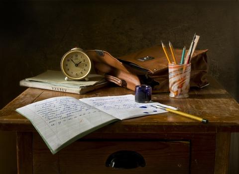 a dark background with an open book and various writing and studying materials