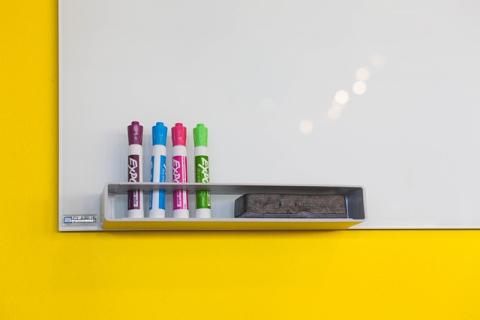 yellow background with a whiteboard and four dry erase markers shown in the corner