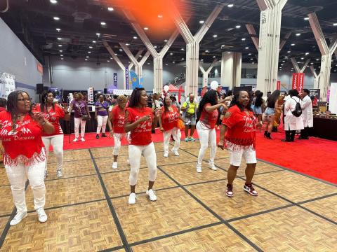 Photo image of what appears to be a gymnasium floor and rows of Black women standing poised to dance