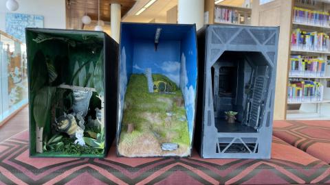 Three book nooks. One depicting where the wild things are, one a house on a hill, and one Grogu in a dark room.