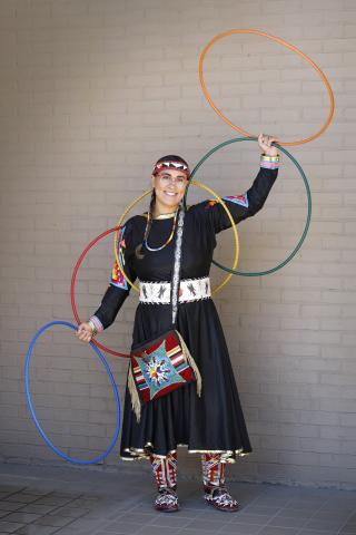 A photo of Starr Chief Eagle in traditional regalia holding four hoops in the air