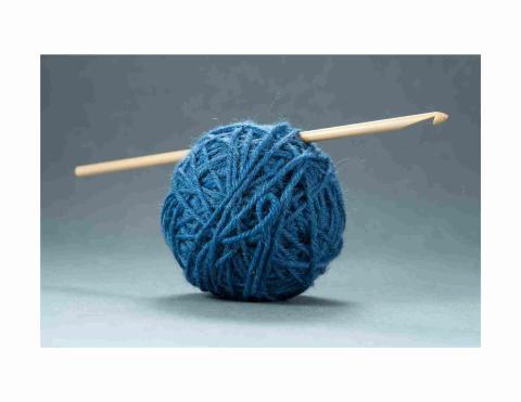 Ball of blue yarn containing a wooden crochet hook.