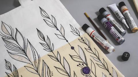 a white and tan canvas with black line drawings of flowers, next to tubes of black paint