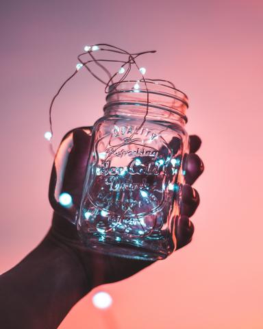 Photo of a hand holding up a mason jar with a strand of LED lights coiled up inside and spilling out.