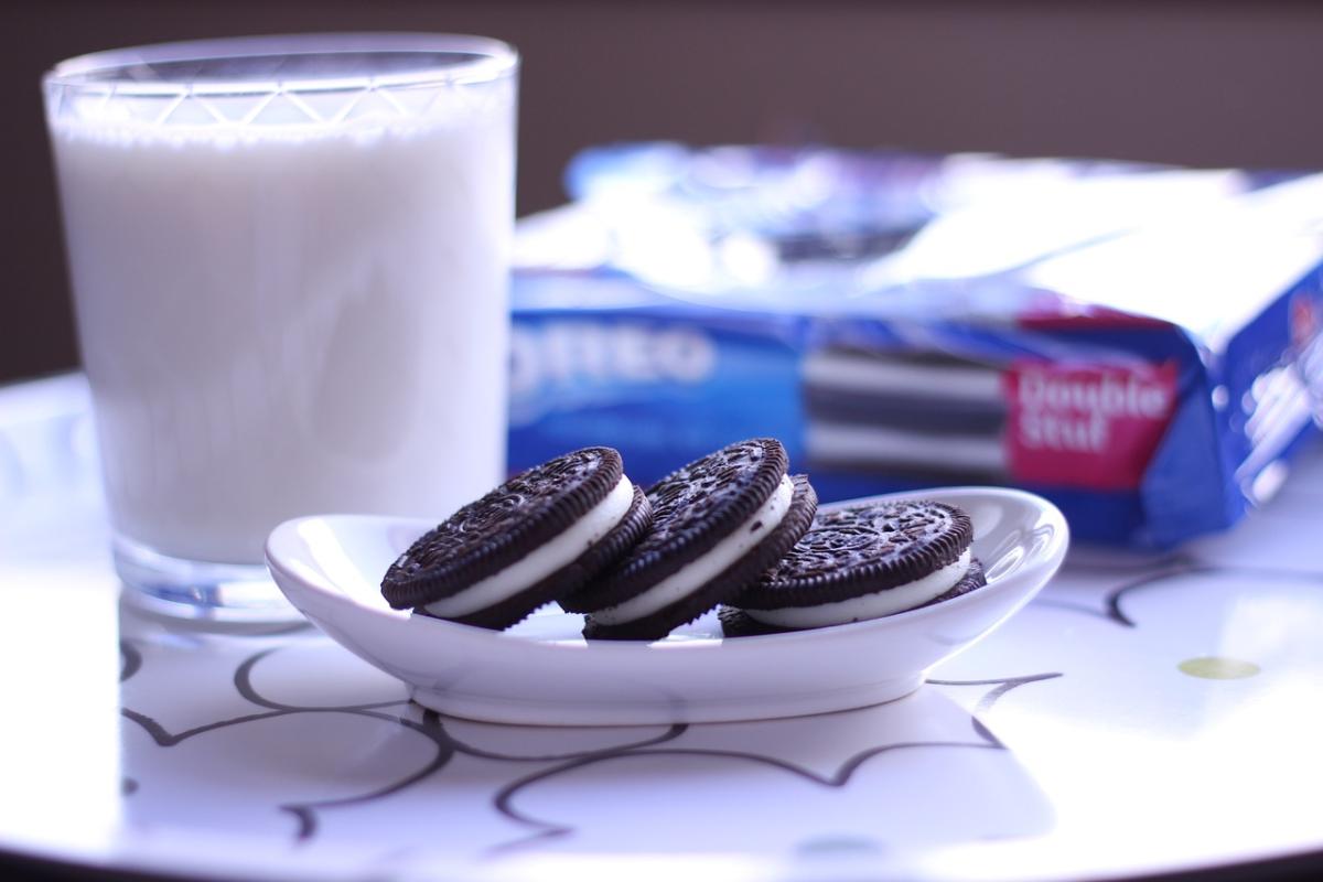 a glass of milk with a dish containing three oreo cookies, and a package of oreos in the background