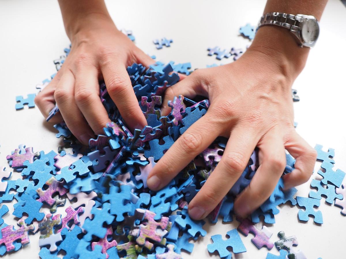 A pair of hands grabbing at a pile of blue puzzle pieces