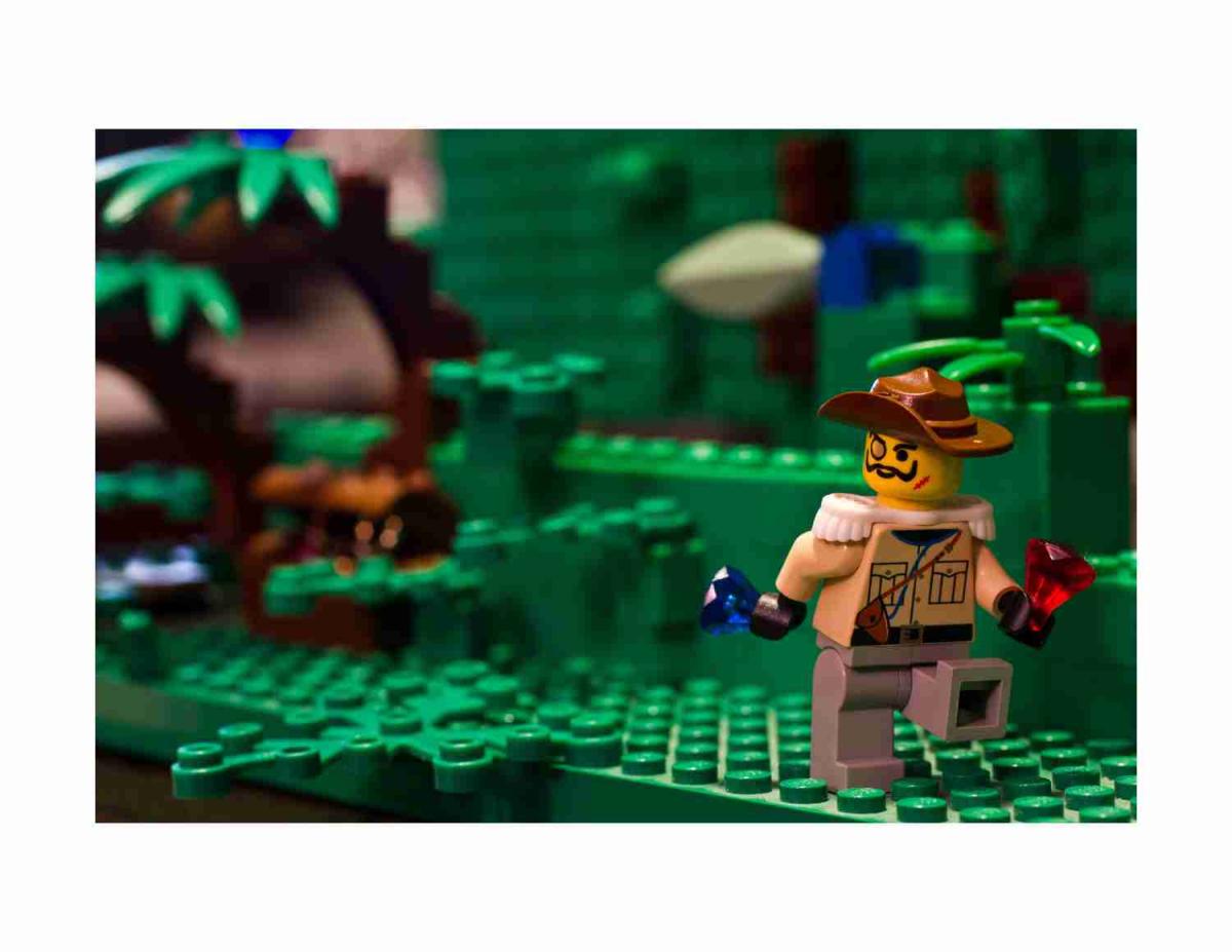 LEGO mini figurer wearing an explorer outfit and holding two diamonds, one red and one blue. The background appears to be a jungle.