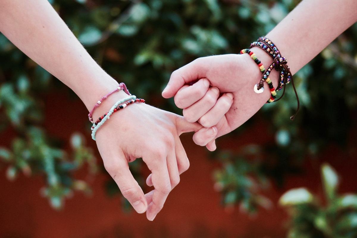 two hands hooking pinkies in front of a green leafy background