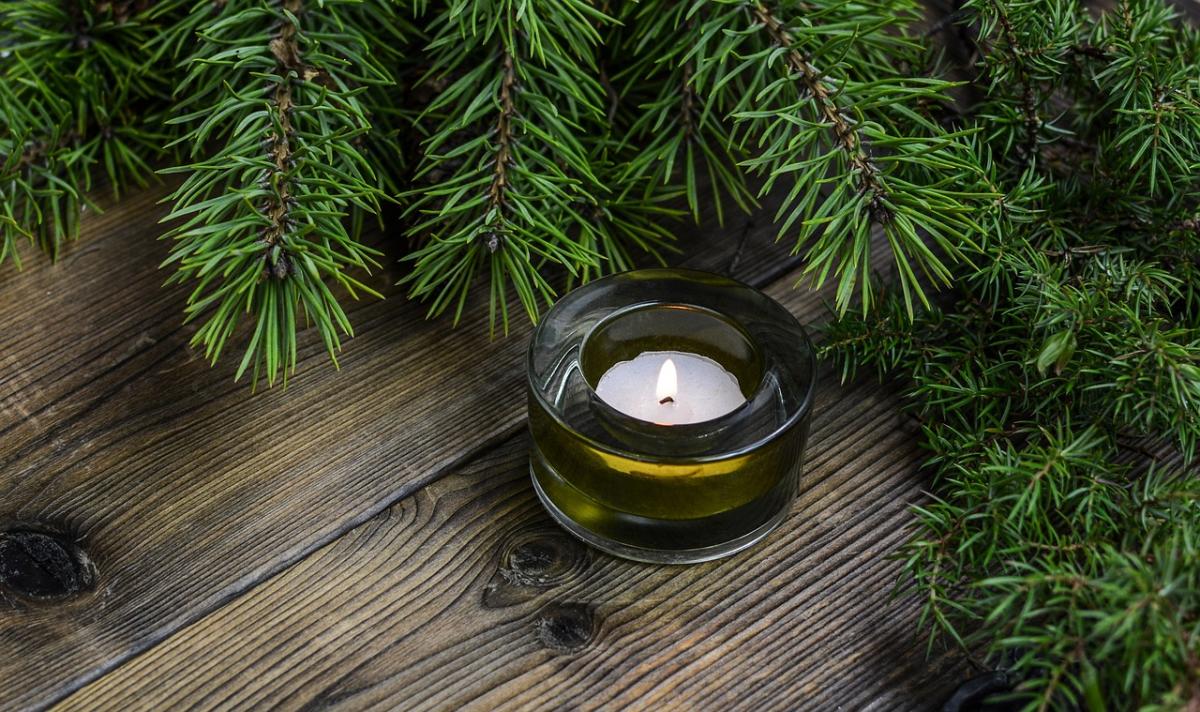 a small white candle sits on a wooden surface surrounded by pine branches