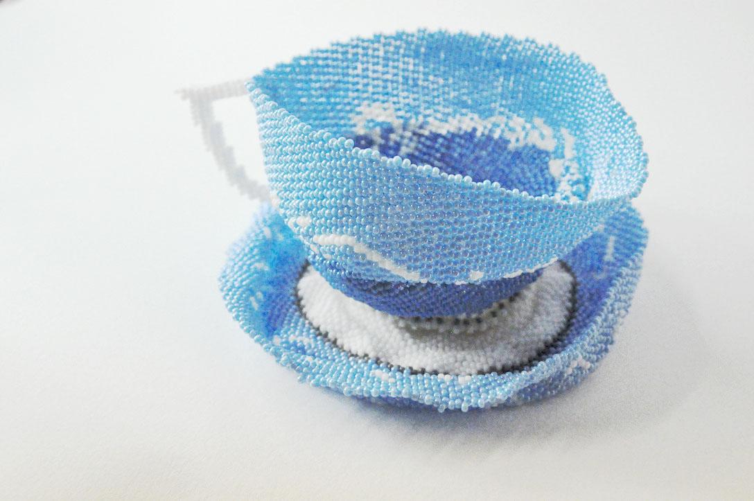 a tea cup made of beads in different shades of blue against a white background