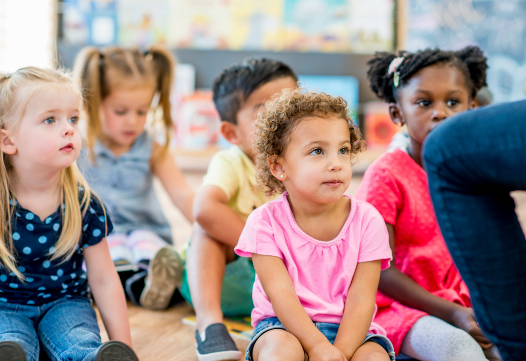 Photo of a diverse group of preschoolers sitting on the floor listening to a story